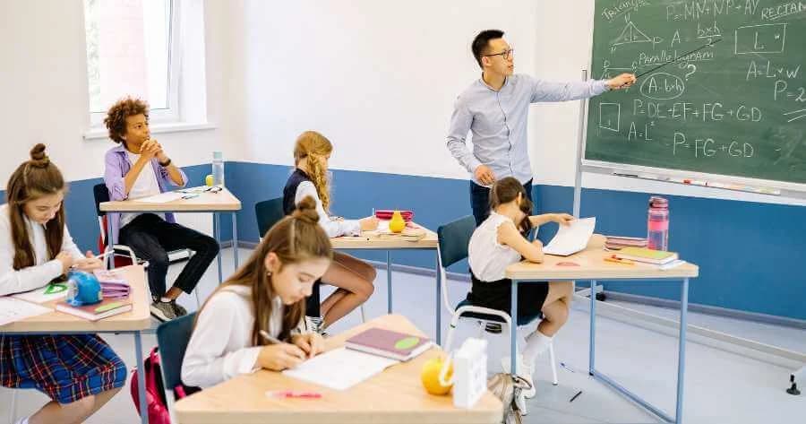 Crianças em sala de aula, incluindo aluno com autismo, participando de atividade baseada em plano de aula adaptado com recursos visuais e apoio individualizado.