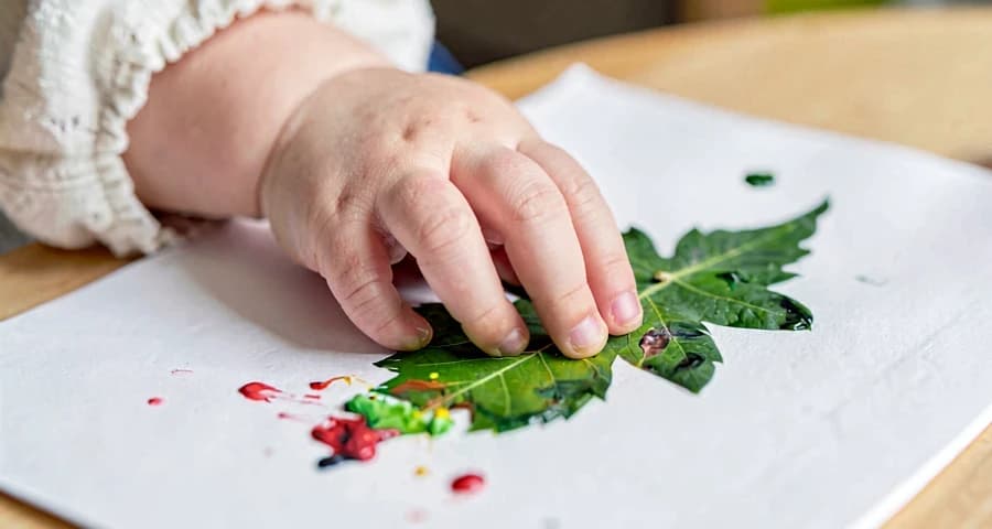 mão de bebê carimbando folha com tinta em atividade artística na creche