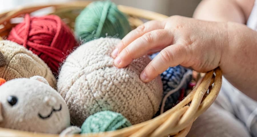 bebê tocando objeto de textura macia em cesta sensorial na creche