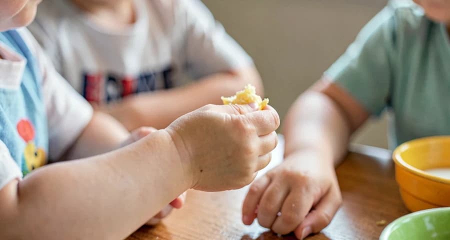 criança da creche compartilhando alimento com colega durante lanche comunitário