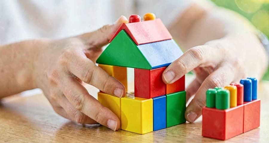 mãos de criança encaixando blocos coloridos para construir casinha na creche