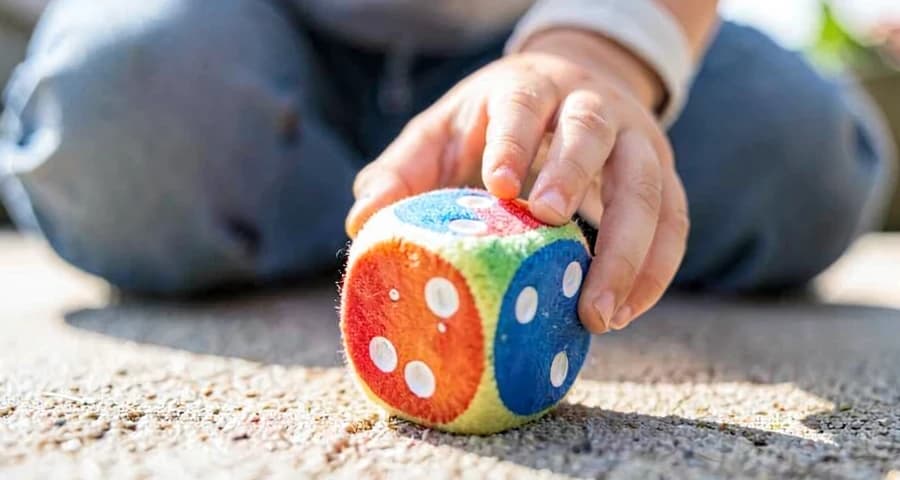 criança da creche jogando dado colorido durante atividade motora