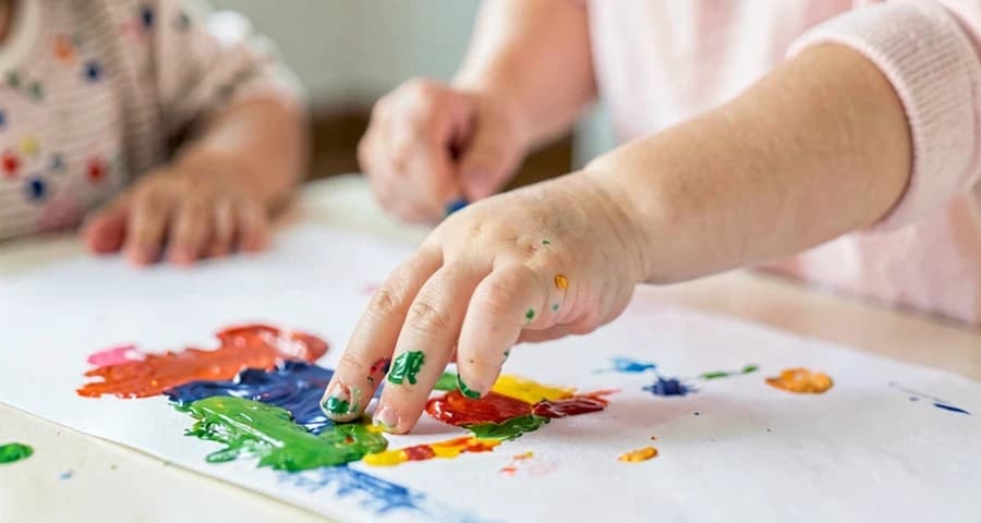 educadora auxiliando bebê a criar marca pessoal com tinta na creche