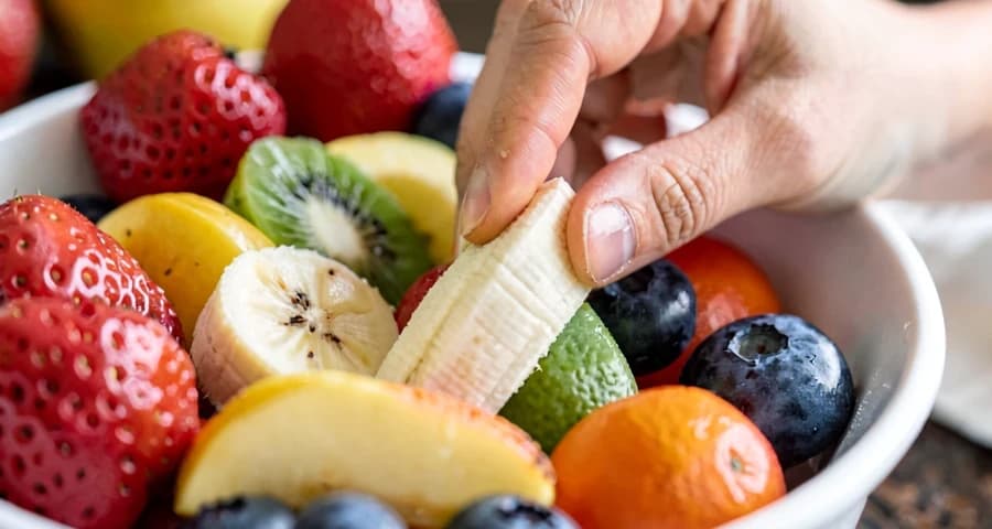 criança da creche colocando fruta em tigela durante atividade culinária