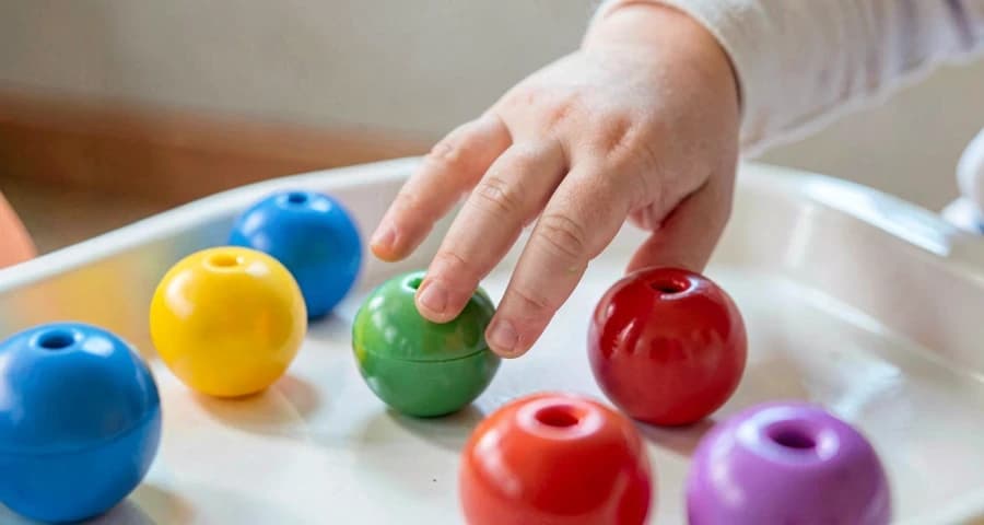 mão de bebê escolhendo objeto sensorial em atividade de autonomia na creche