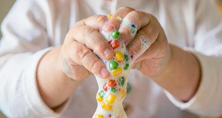 mão de bebê apertando massa sensorial colorida em atividade na creche